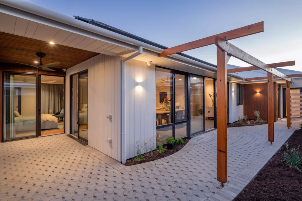 Outdoor patio area with wooden deck, glass doors, and seating under soft evening lighting.
